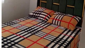 Una cama con una colcha a cuadros y dos almohadas, un cuadro enmarcado en la pared y una ventana con persianas.