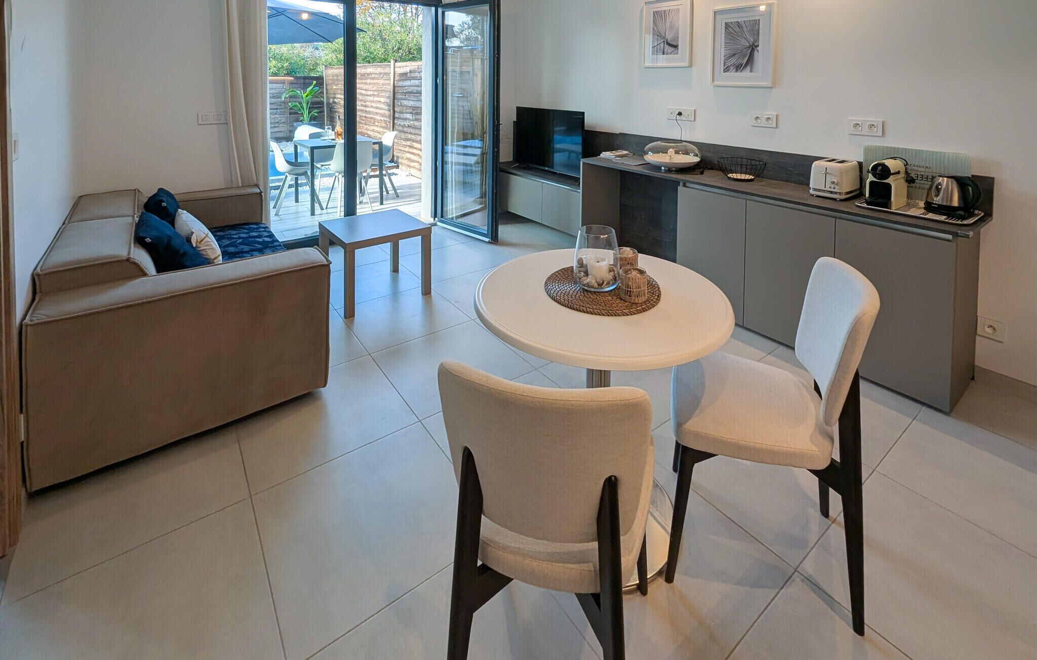 A modern living room with a sofa, two chairs, a small table, and a kitchen area with a TV and appliances.