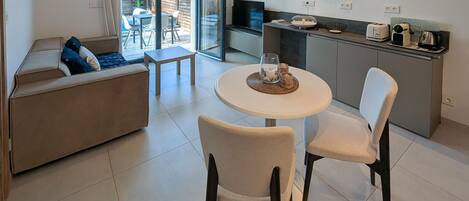 A modern living room with a sofa, two chairs, a small table, and a kitchen area with a TV and appliances.