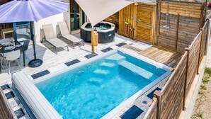 A rectangular swimming pool with a wooden deck surrounding it, a hot tub, and a covered seating area with a table and chairs. - Stunning home in Roquefort Les Pins (Roquefort Les Pins)