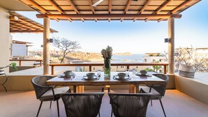 A covered outdoor dining area with a table set for four, overlooking a scenic coastal view. - Private Oceanfront Rooftop Plunge Pool & Beach Access (Huatulco)
