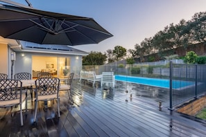 Un espacio al aire libre cubierto con piscina, una mesa de comedor con sillas y un paraguas grande.