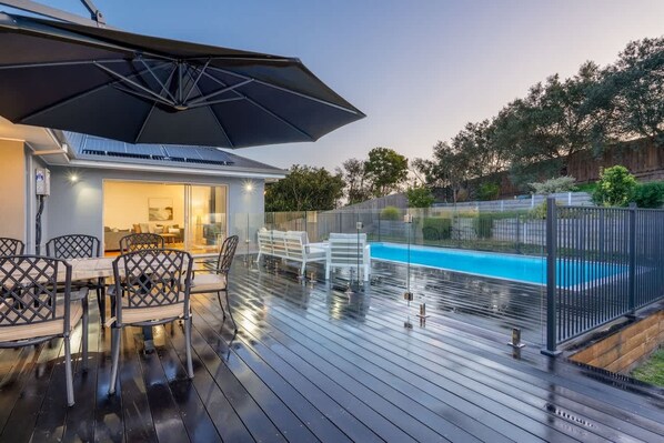 A covered outdoor area with a pool, a dining table with chairs, and a large umbrella.