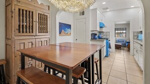 Een keuken met een houten tafel en bankjes, een decoratieve plafondlamp en uitzicht op de woonkamer.