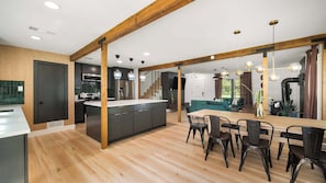 Una cocina moderna con una isla central, vigas de madera y un comedor con una mesa grande y sillas.