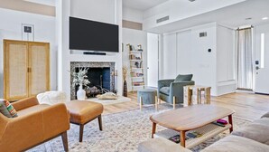 Een ruime woonkamer met een open haard, een flatscreen televisie en een boekenkast.