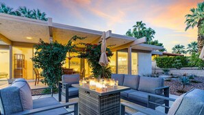 Een terras buiten met een vuurplaats, modern meubilair en uitzicht op het huis.