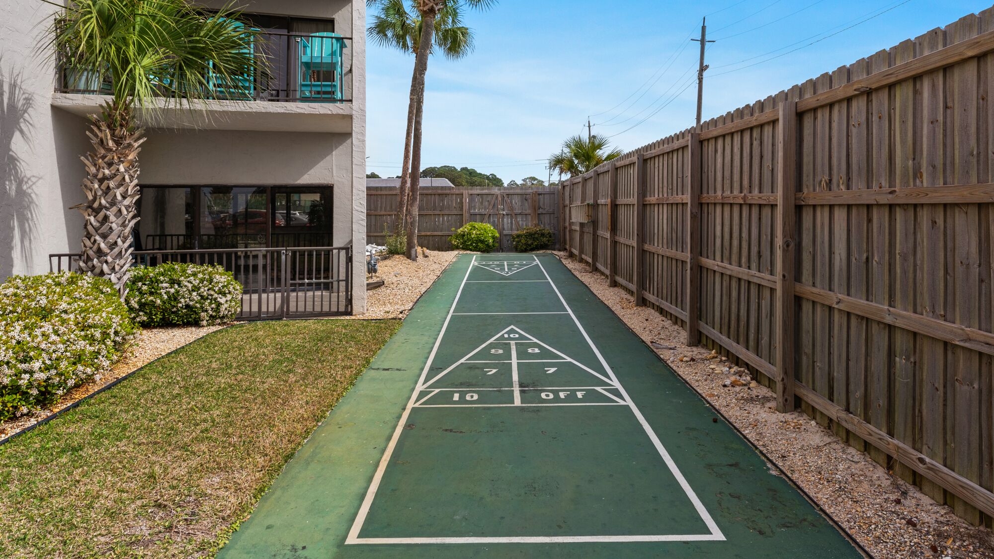 A shuffleboard court with a wooden fence and a building with balconies.