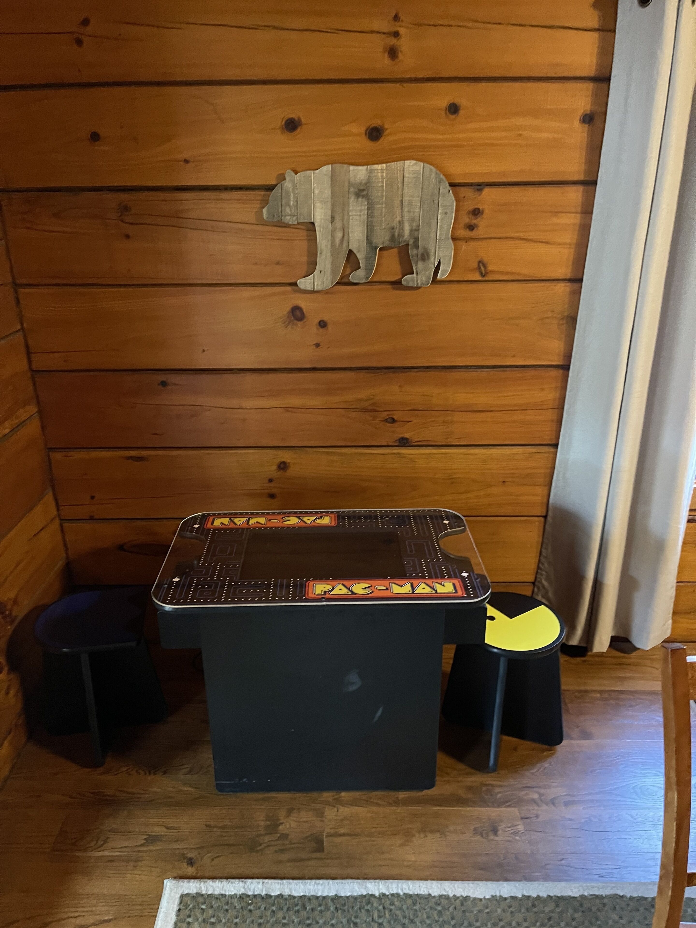A Pac-Man arcade game on a wooden table with a bear decoration on the wall.