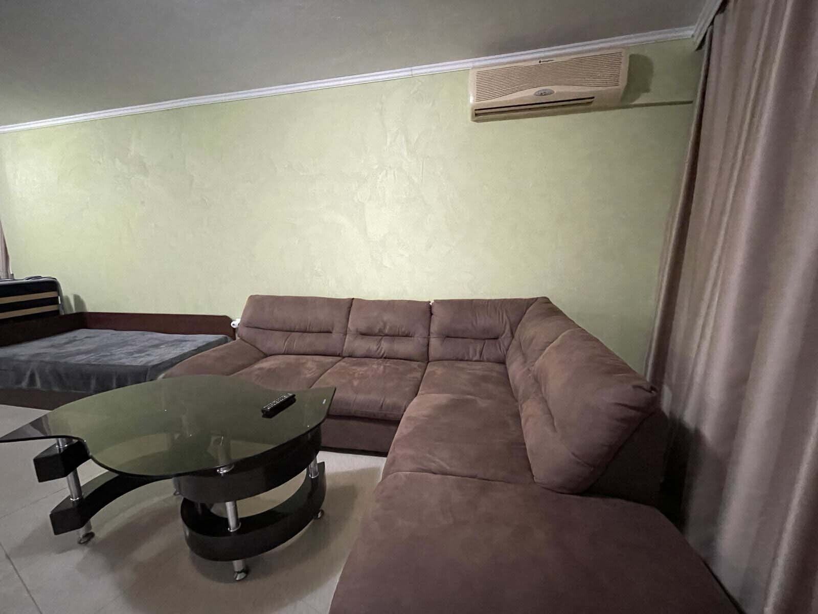 Una sala de estar con un sofá modular, una mesa de centro de vidrio y un aire acondicionado instalado en la pared.