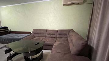 Una sala de estar con un sofá modular, una mesa de centro de vidrio y un aire acondicionado instalado en la pared.