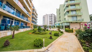 A courtyard with a paved walkway, surrounded by multi-story buildings with balconies and large windows. - Apart hotel Gallery A
Апартамент в Слънчев Бряг на първа линия-гледка море (Слънчев бряг)