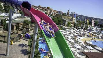 A water park with a multi-colored water slide, inflatable rafts, and a pool area with umbrellas.