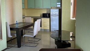 A hotel room with a bed, a dining table with chairs, a kitchen area with cabinets and appliances, and a window with curtains. - Apart hotel Gallery A
Апартамент в Слънчев Бряг на първа линия-гледка море (Слънчев бряг)