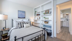 A bedroom with a bed, bedside tables, a nightstand, and a wall-mounted shelf with decorative items. - 30+ Day 3BR Home One Blk off Historic Main St. Galena w/Pking and W/D (Galena)