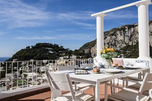 A terrace with a table set for dining, overlooking a coastal town and a mountainous backdrop. - Casa Luna Caprese - Capri Center (Capri)