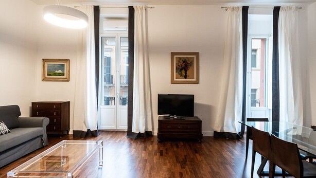 Una sala de estar moderna con sofá, televisor, mesa de centro de vidrio y zona de comedor.
