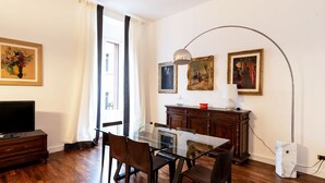 Un comedor con una mesa de vidrio, sillas de madera, un armario de madera oscura y un televisor sobre un mueble.