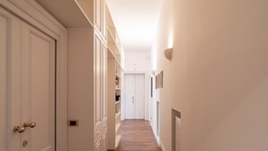 Un pasillo estrecho con paredes blancas y suelo de madera, que conduce a una puerta con un buzón pequeño.