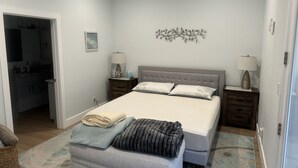 Un dormitorio con cama, dos mesitas de noche, ventilador de techo, una obra de arte en la pared y un baño visible a través de una puerta abierta.