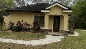 Una casa de un piso con fachada amarilla, techo oscuro y entrada principal con puerta de vidrio.