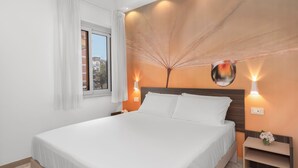 A neatly made bed in a hotel room with a large window, two wall-mounted lights, and a nightstand with a vase of flowers. - Large Apartment in the Center of Sorrento, close to Main Transportation Hubs. (Sorrento)