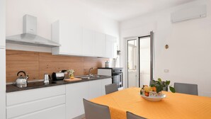 A modern kitchen with white cabinets, a stainless steel range hood, and a wooden backsplash. There is a dining table with an orange tablecloth and a bowl of fruit. - Large Apartment in the Center of Sorrento, close to Main Transportation Hubs. (Sorrento)