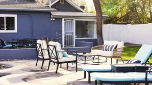Un patio con mobiliario exterior, un área de estar cubierta y una casa al fondo.