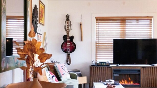 Una sala de estar con sofá, televisión, chimenea y guitarra.