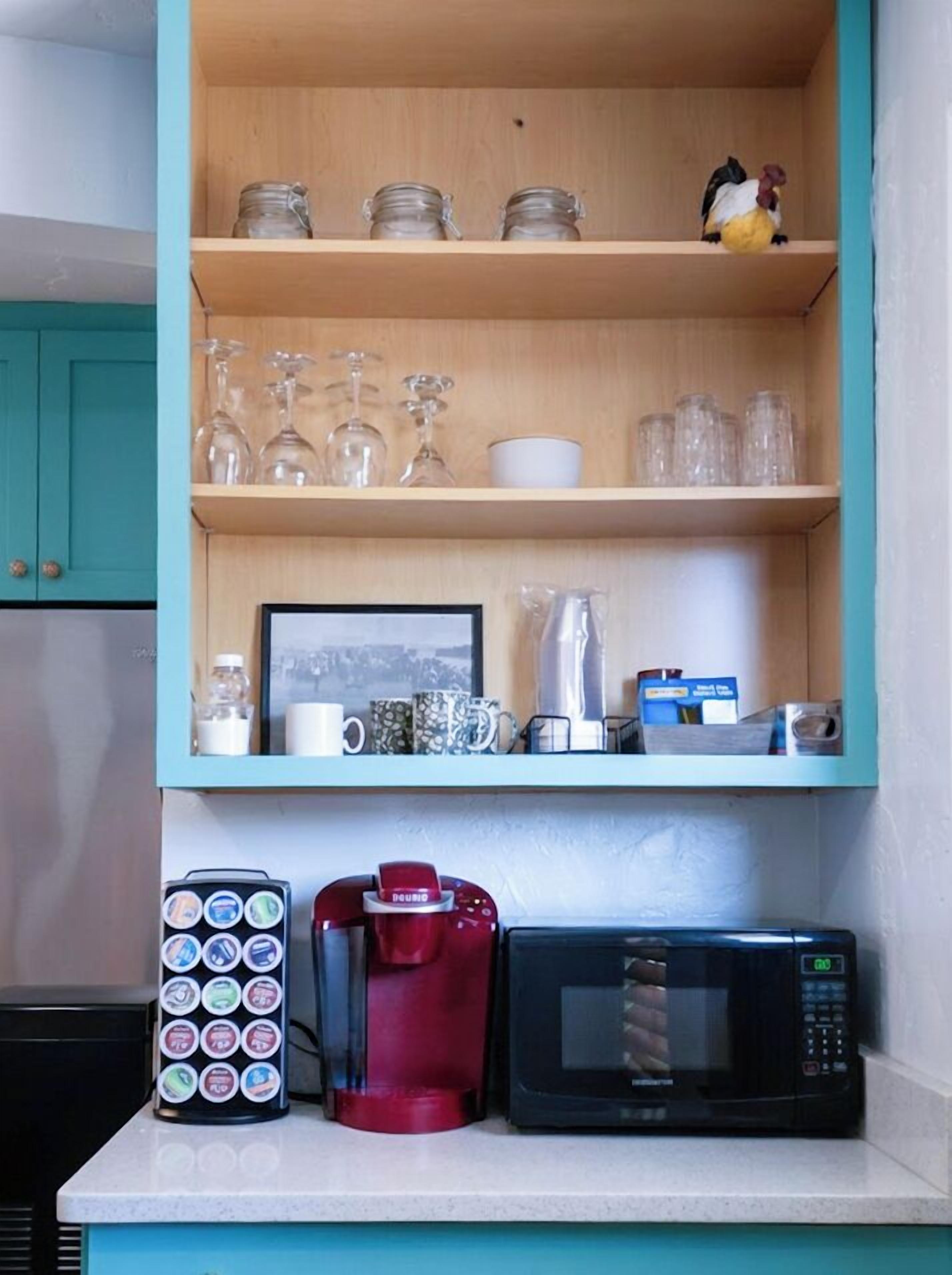 Une cuisine avec un meuble de couleur turquoise contenant de la verrerie, une machine à café et un four à micro-ondes.