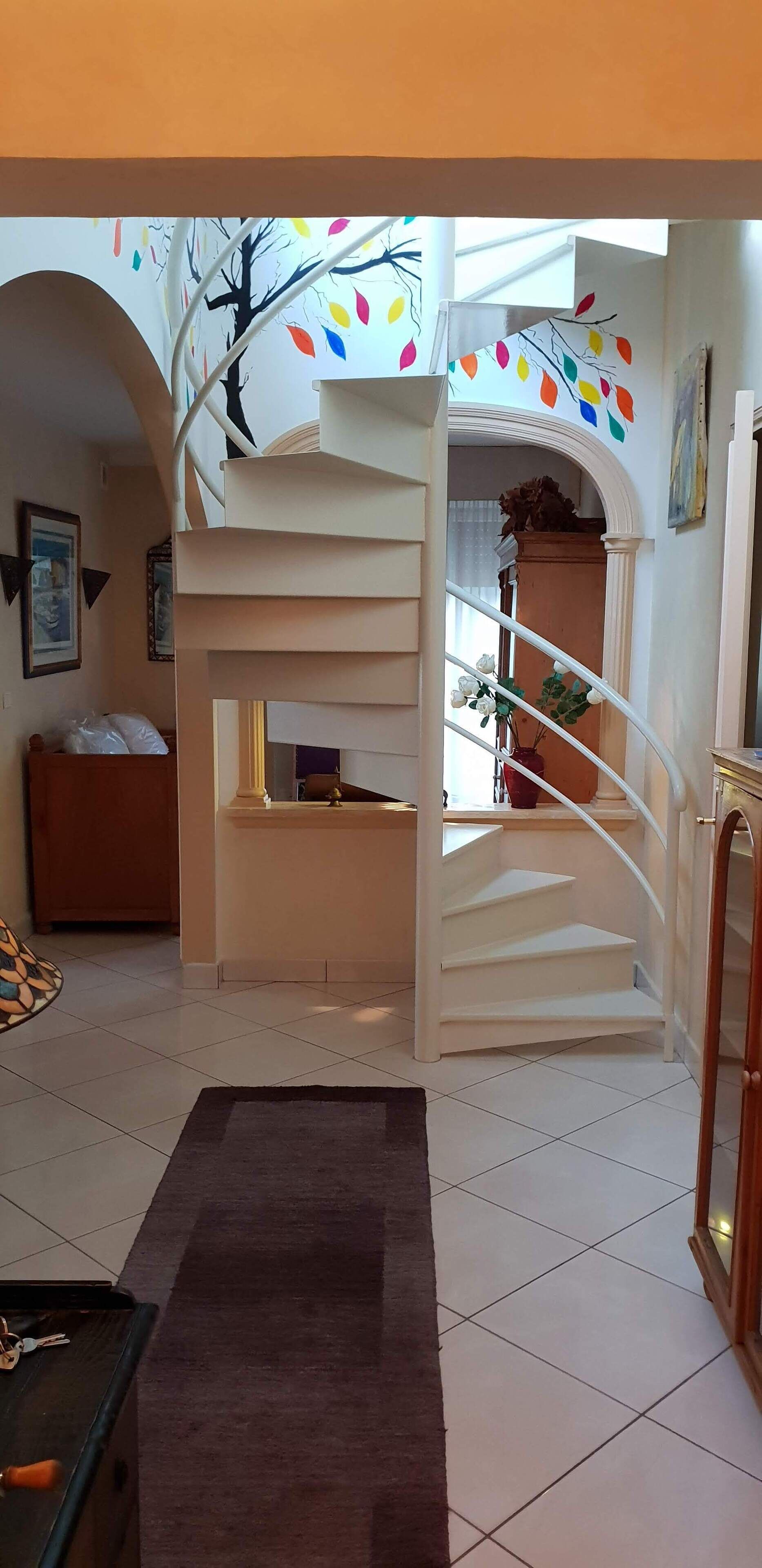Una escalera con barandilla blanca que lleva a una plataforma, un sofá marrón y una mesita con llaves encima.