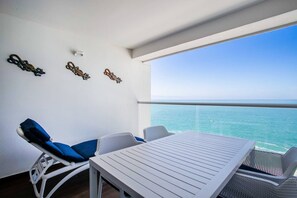 En balkon med et bord og stole, havudsigt og dekorativ vægkunst.