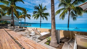A poolside area with lounge chairs, palm trees, and a view of the ocean.
