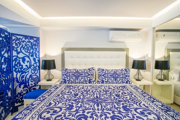 A bedroom with a large bed, two bedside tables, a blue decorative panel, and an air conditioning unit on the wall.