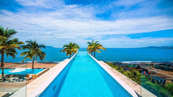 Una larga piscina con agua cristalina azul, rodeada de palmeras y vistas al océano.