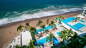 A beachfront hotel with a pool area, palm trees, and ocean views. - 11th-Floor Oceanview Stay | Infinity Pools + Gym (Puerto Vallarta)