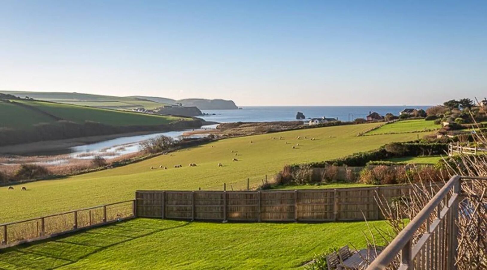 A coastal landscape with a fenced field, a body of water, and distant hills.