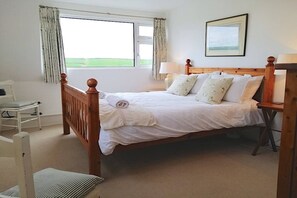 Ein Schlafzimmer mit einem hölzernen Bett, weißer Bettwäsche, einem Sessel, einem Nachttisch und einem Fenster mit Vorhängen.