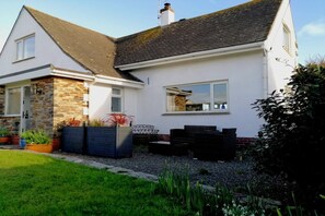 A two-story house with a stone facade, a tiled roof, and a garden with potted plants and outdoor furniture. - Sea Reach, Thurlestone, sleeps 8 (Thurlestone)