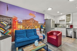 A modern living room with a blue sofa, a red chair, and a coffee machine in the kitchen area.