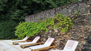 A poolside area with lounge chairs and a stone wall. - Family manor house  (Bouchemaine)