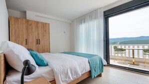 A bedroom with a bed, a wooden wardrobe, a desk with a lamp, and a balcony with chairs. - 5 Comfort Studio Apartment (Neum)