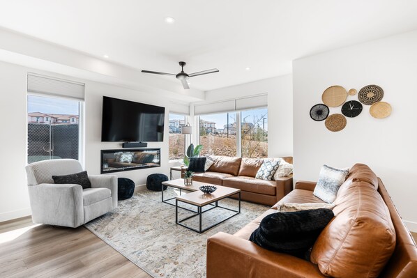A modern living room with a large TV, leather sofas, a coffee table, and a ceiling fan.