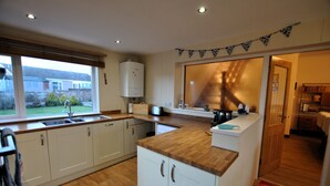 A kitchen with white cabinets, a wooden countertop, and a window overlooking a backyard. - Stronvar- coastal home with sea views (Pittenweem)