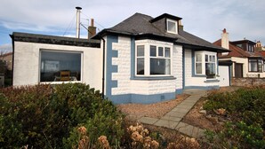 A two-story house with a large bay window, a chimney, and a garden with shrubs and dried flowers. - Stronvar- coastal home with sea views (Pittenweem)