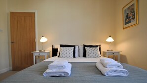 A neatly made bed with two pillows, two nightstands with lamps, and a door. - Stronvar- coastal home with sea views (Pittenweem)