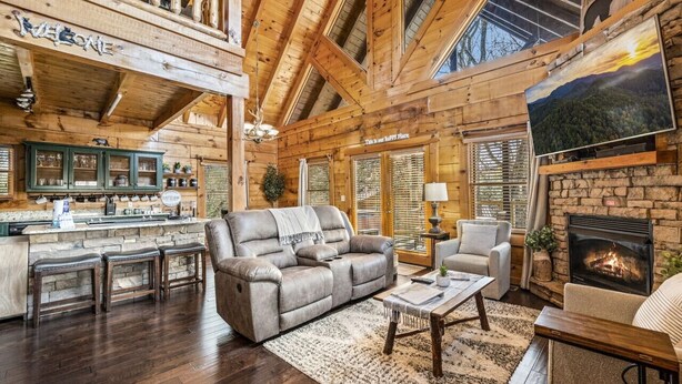 A cozy cabin interior with a fireplace, wooden beams, a bar area, and a comfortable seating arrangement. - Near Attractions-Pool Table-Hot Tub-Fire Pit (Pigeon Forge)