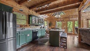 A spacious wooden cabin with a large kitchen featuring green cabinets, a stainless steel refrigerator, and a bar area. - Near Attractions-Pool Table-Hot Tub-Fire Pit (Pigeon Forge)