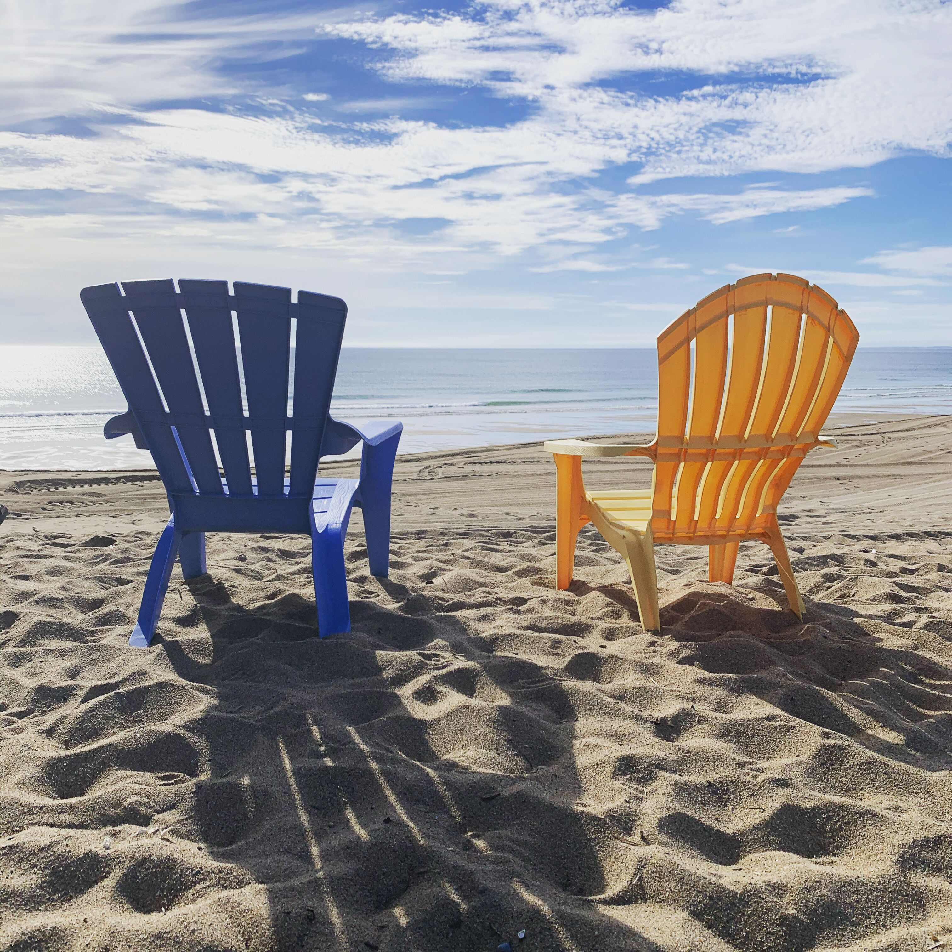 Deux chaises de plage sur une plage de sable, avec vue sur l’océan.