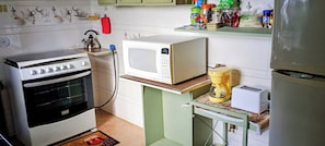 Cozinha com fogão, micro-ondas, cafeteira e diversos utensílios de cozinha nas prateleiras.
